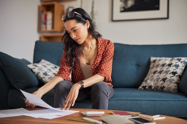 Woman sitting on couch in her house looking at paperwork on her coffee table