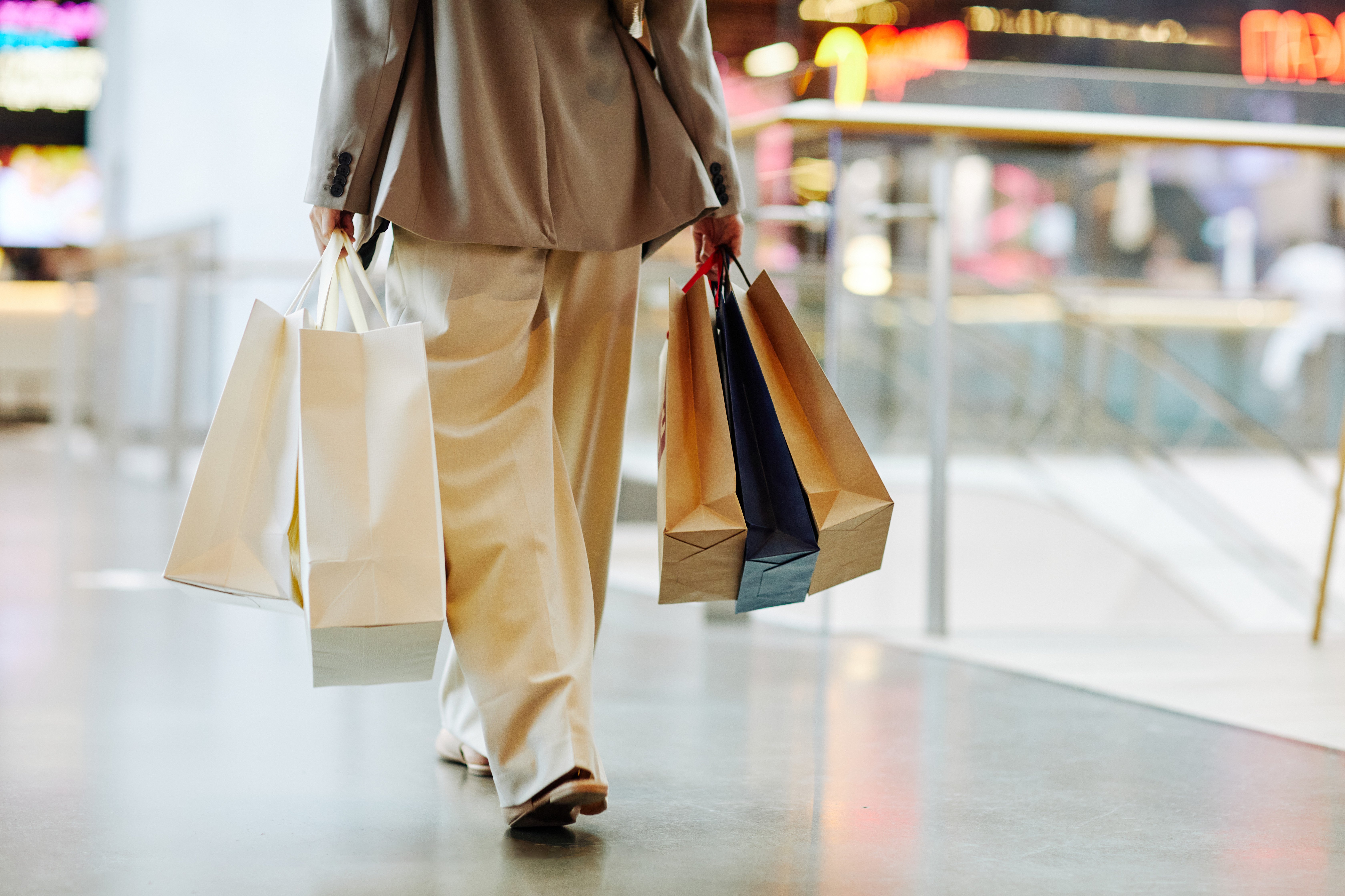 Low section of unrecognizable woman wearing pants and holding blank shopping bags while walking in mall