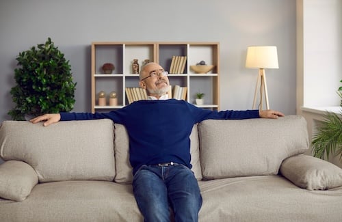 Calm senior grey-haired man sit relax on comfortable sofa furniture at home look in distance dreaming making plans Adobe stock photo