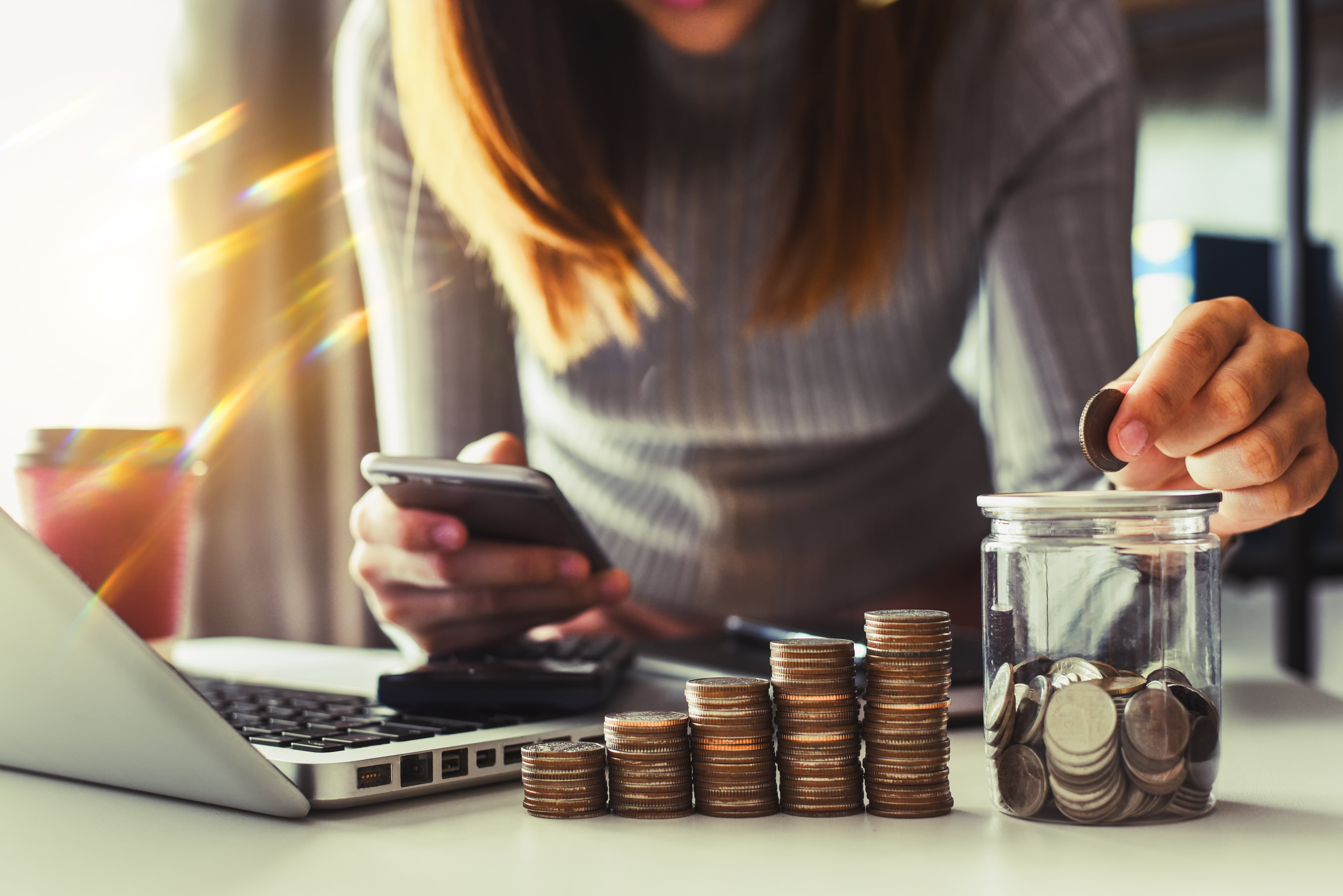 businesswoman holding coins putting in glass with using smartphone and calculator to calculate concept saving money for finance accounting Adobe stock photo