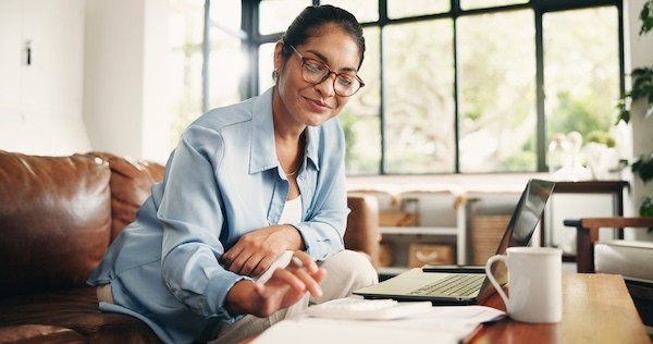 Woman, finance or calculator with laptop in home for budget planning, bills or expenses. Female person, accounting or checklist with documents on sofa