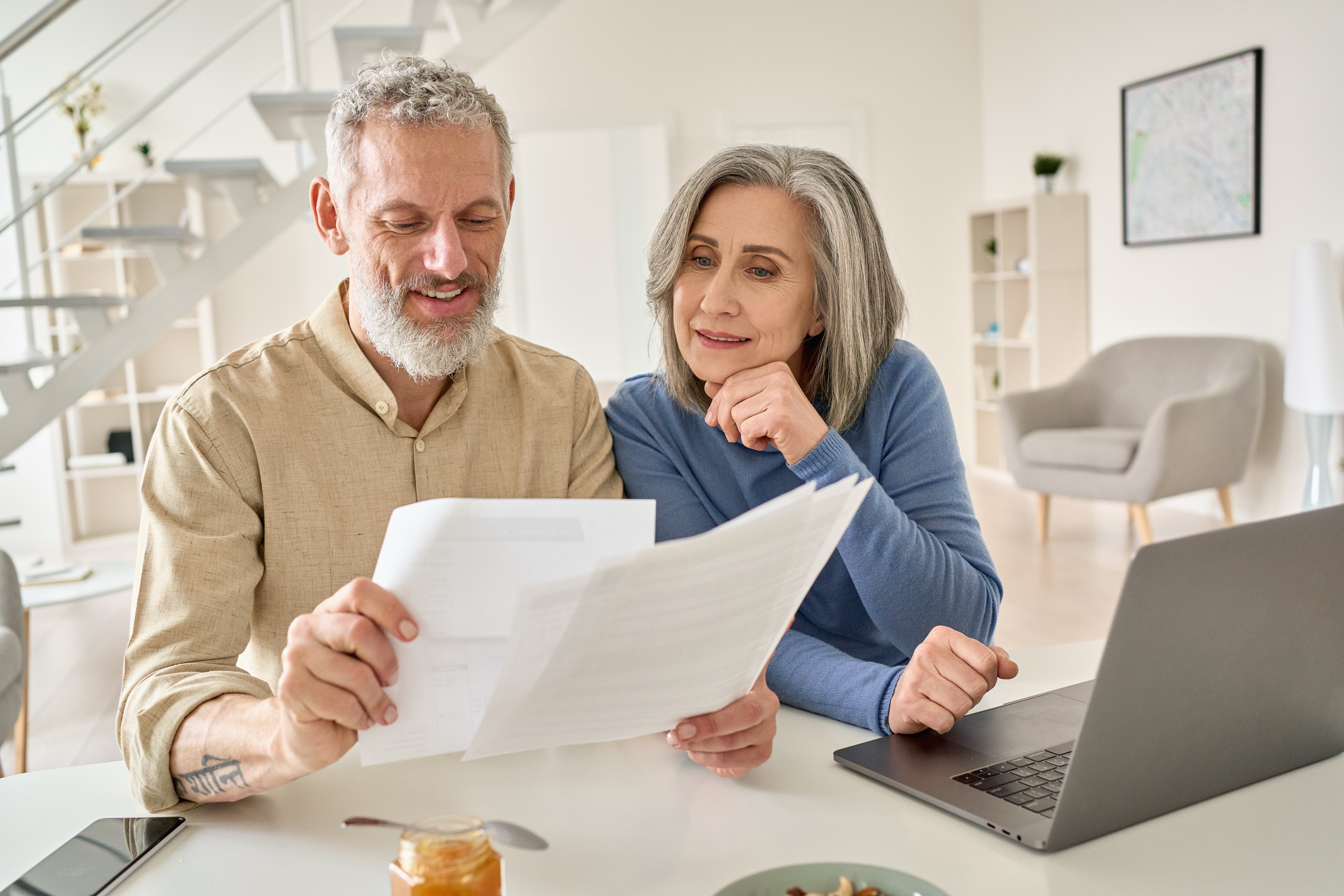 Middle aged senior old couple holding documents reading paper bills paying bank loan online Adobe stock image