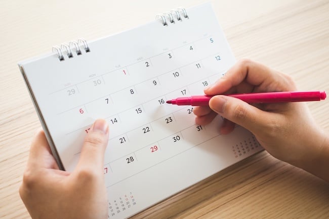 Hand with pen writing on calendar page closeup