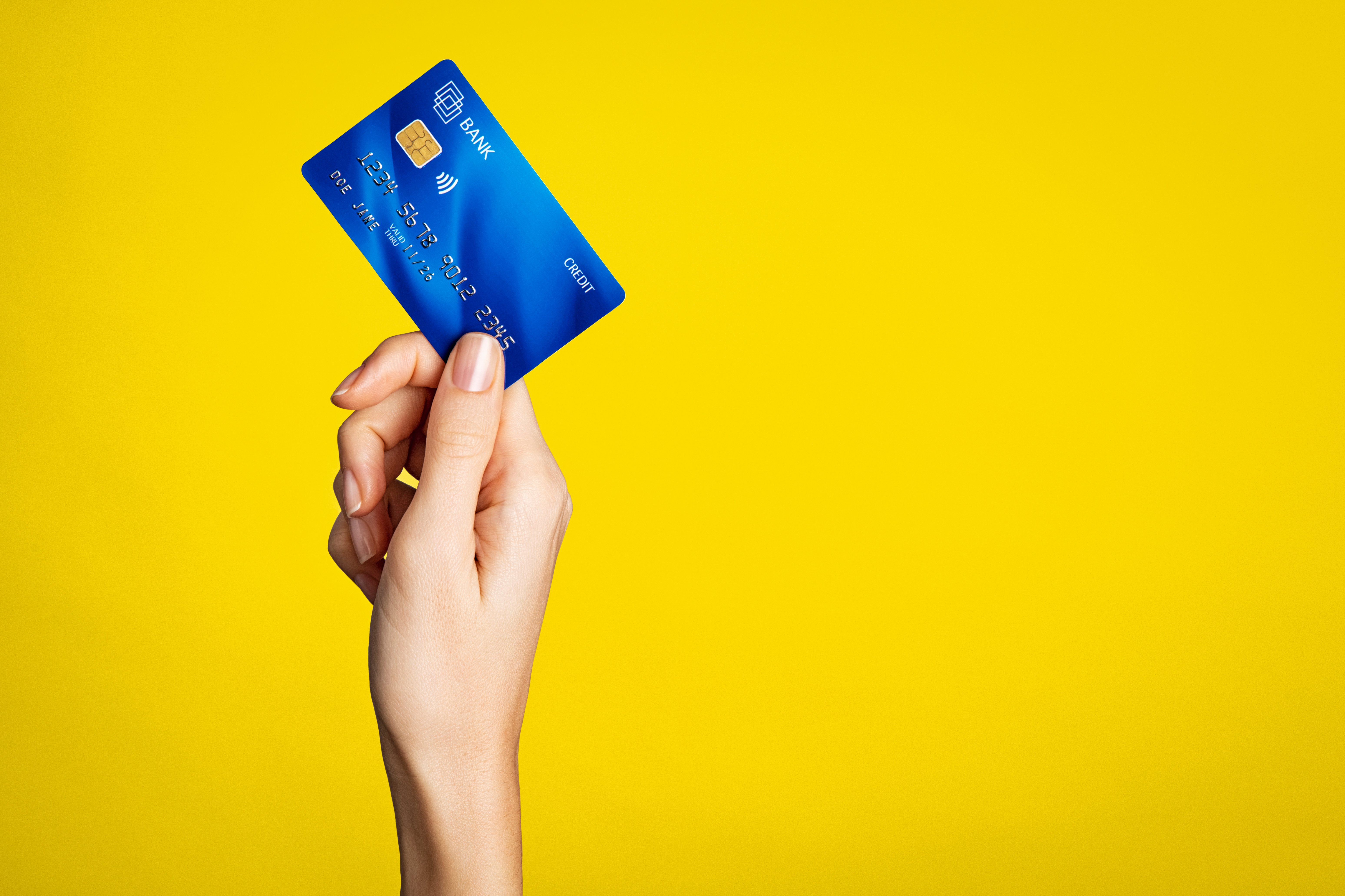 woman's hand holding credit card against yellow background Adobe Stock photo