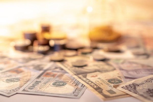 Various of international money coin and banknote with blurred hourglass in the background. Time investment with currency exchange concept. Focus on dollar banknote.