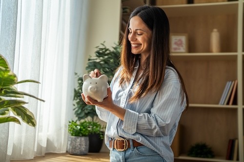 Woman smiling while putting money into piggy bank