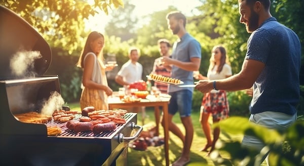 Grilled meat and sausages on the grill with a group of happy friends having dinner party at patio garden fest