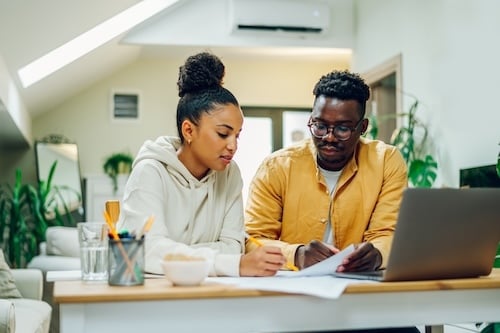 Diverse couple using laptop and looking into the blueprints of their new home
