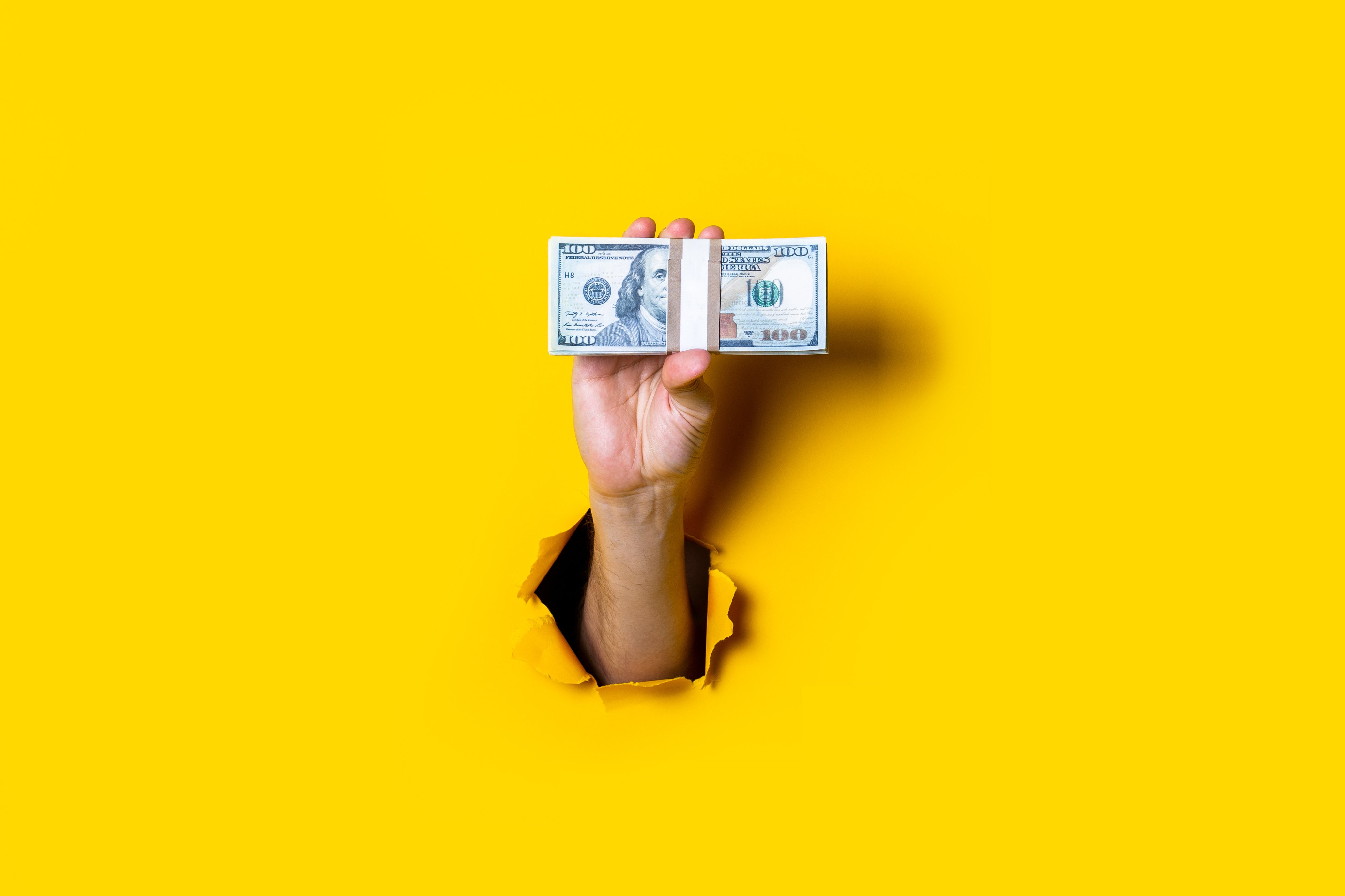 hand holds horizontally a bundle of money bills on a yellow background Adobe Stock photo