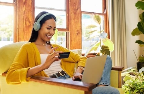 Happy woman, laptop and credit card with ecommerce and headphones to listen to music while online shopping