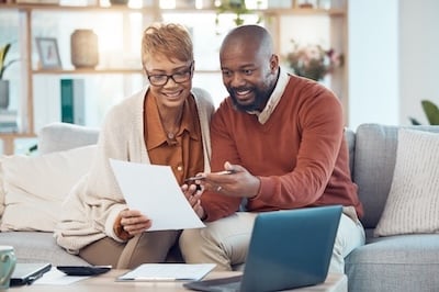 middle aged man and woman do online banking on laptop with documents at home Adobe stock image
