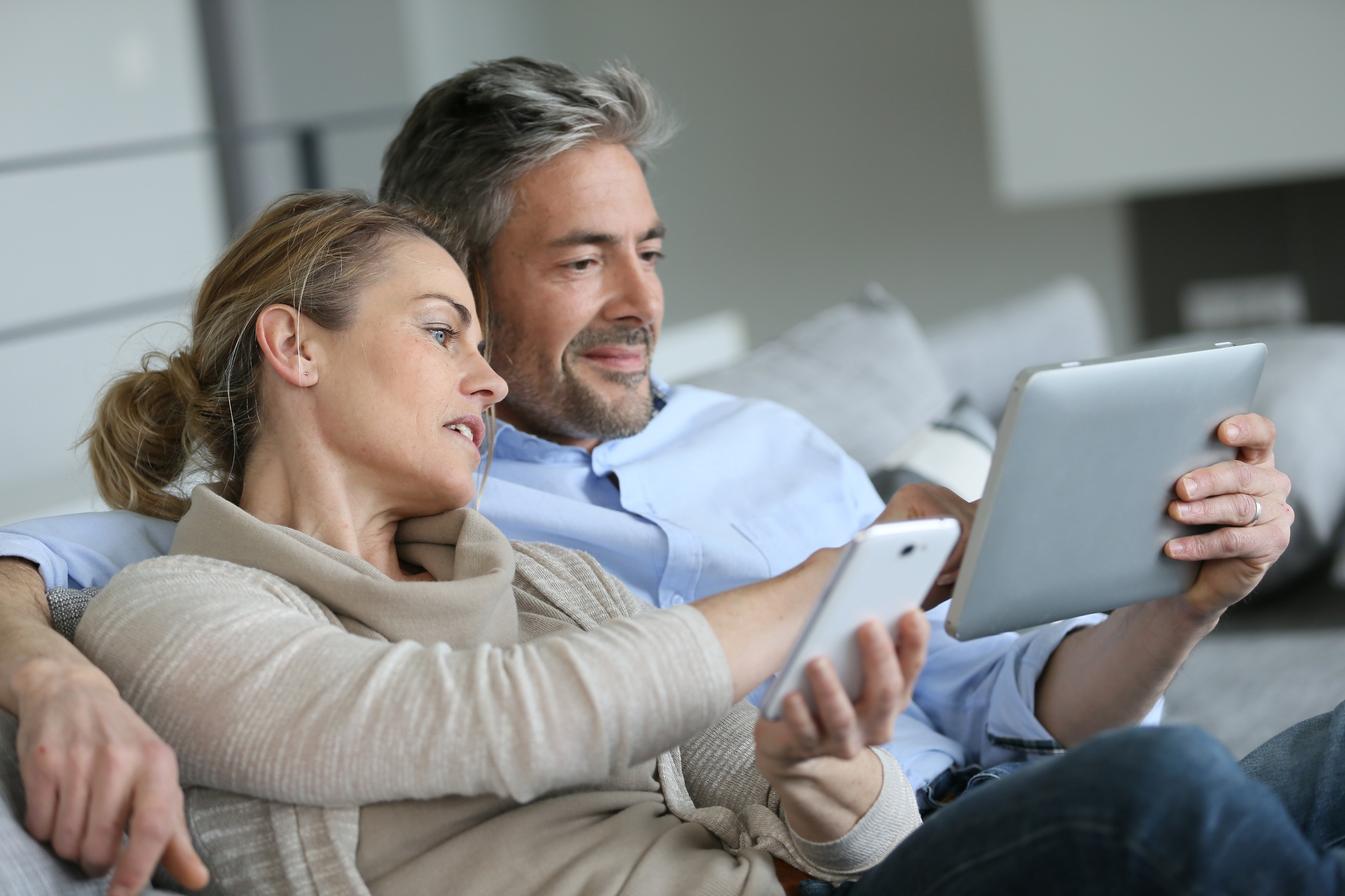 adult couple at home sitting on couch working on ipad and phone Adobe stock images