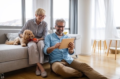 Beautiful happy mature couple is using a digital tablet, talking and smiling at home