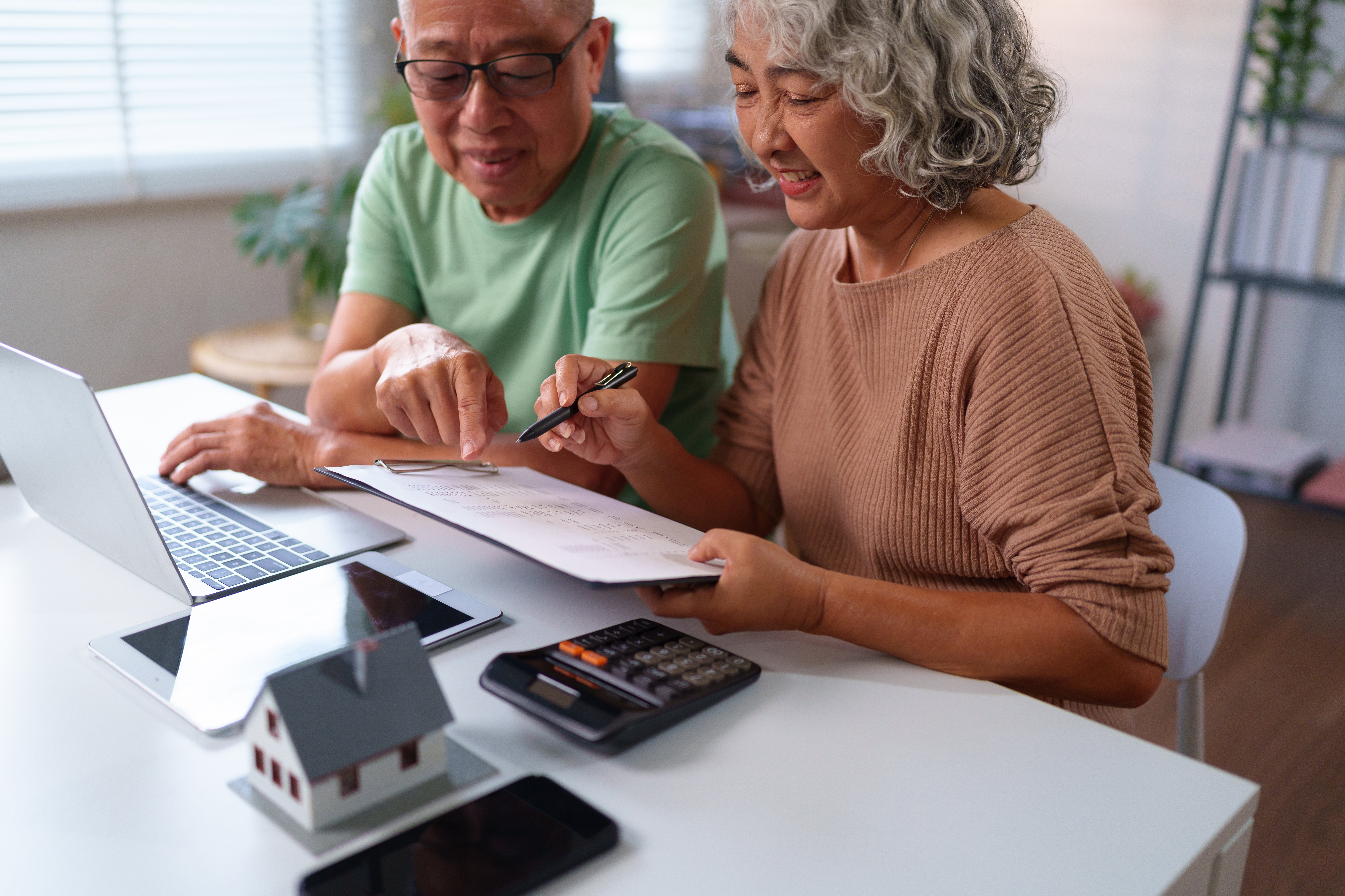 Senior Asian Couple Planning Finances at Home with Laptop, Calculator and Documents