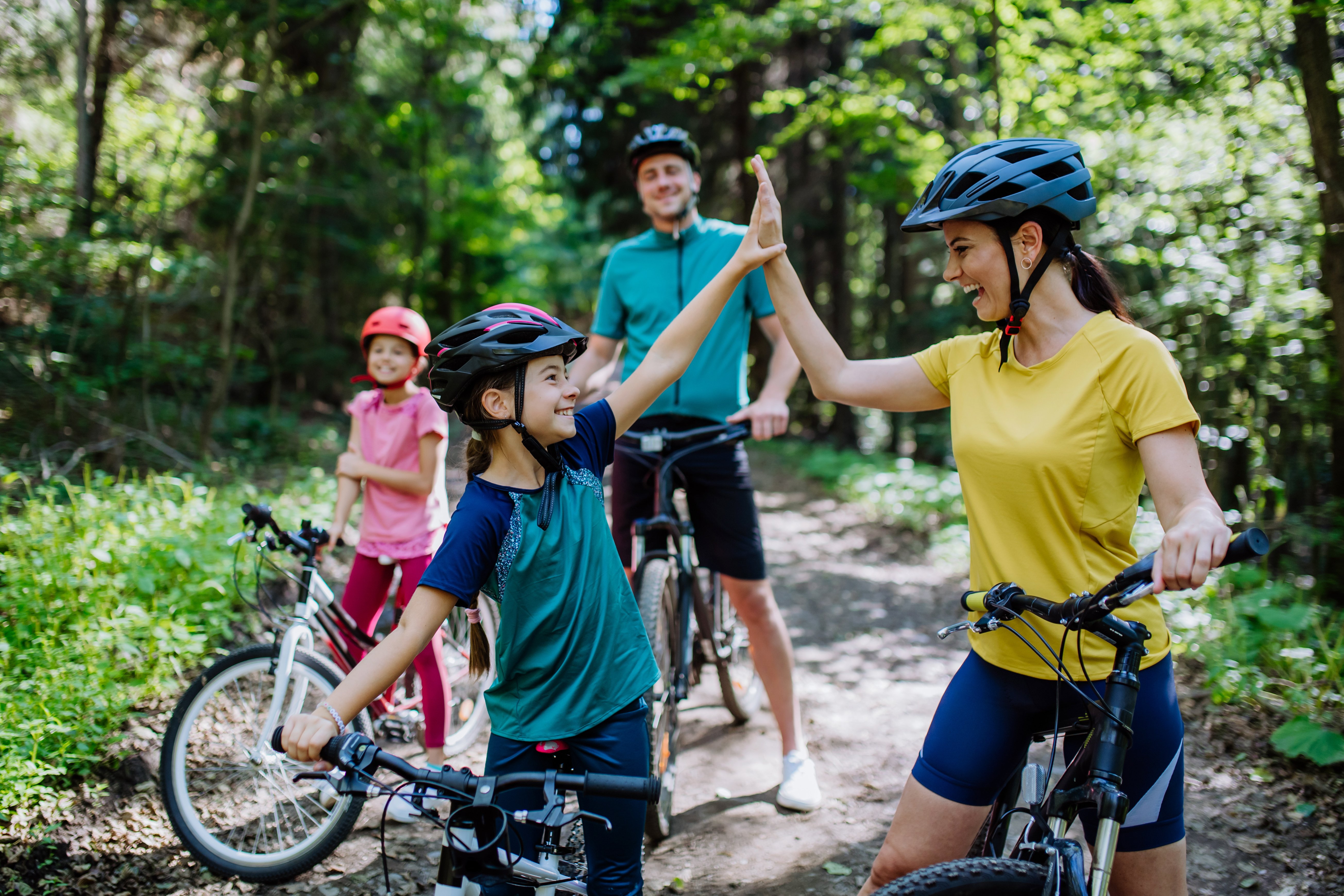 Young family with little children preapring for bike ride, standing with bicycles in nature and high fiving.