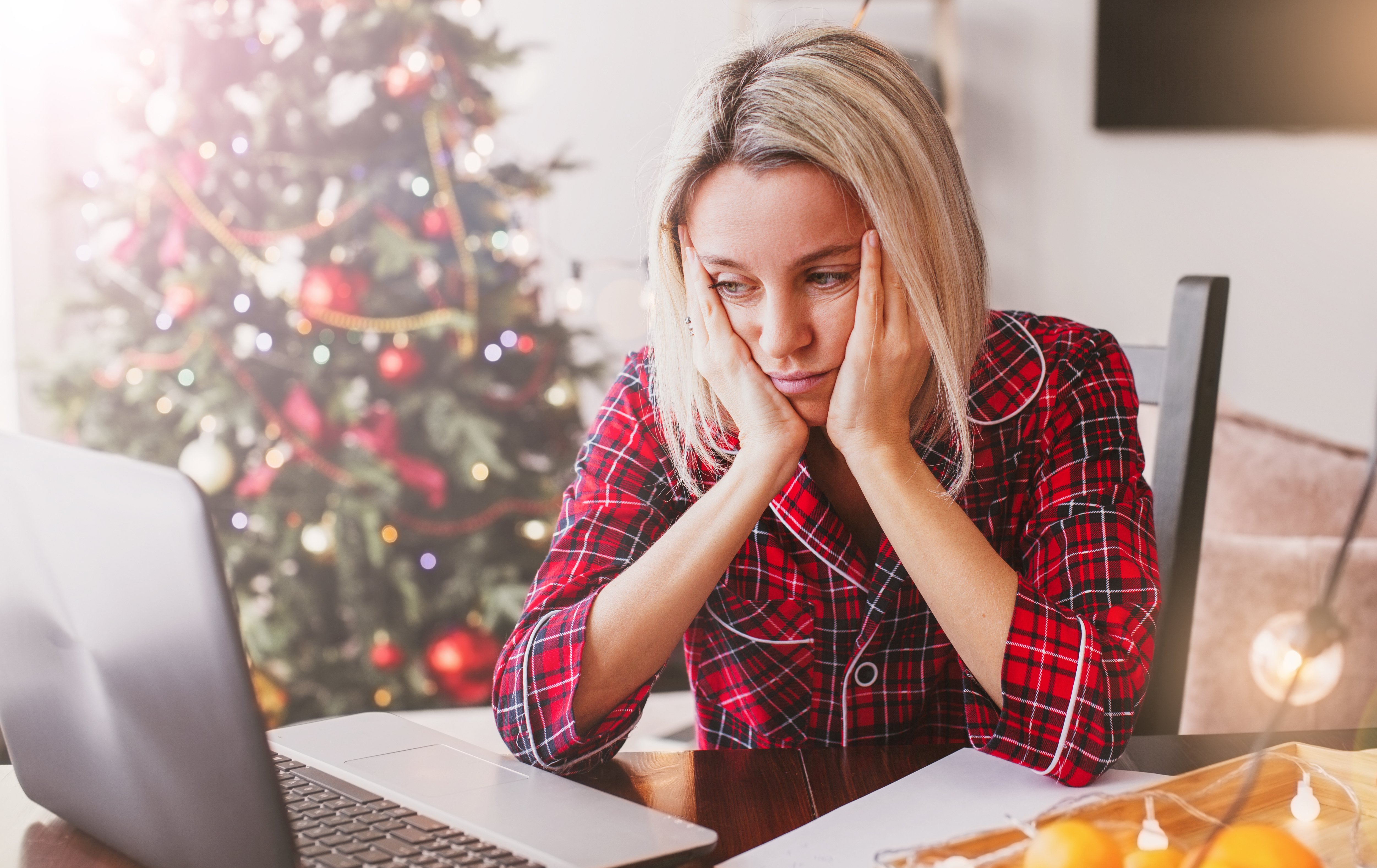 Sad middle aged woman working at the home office by laptop during Christmas holiday