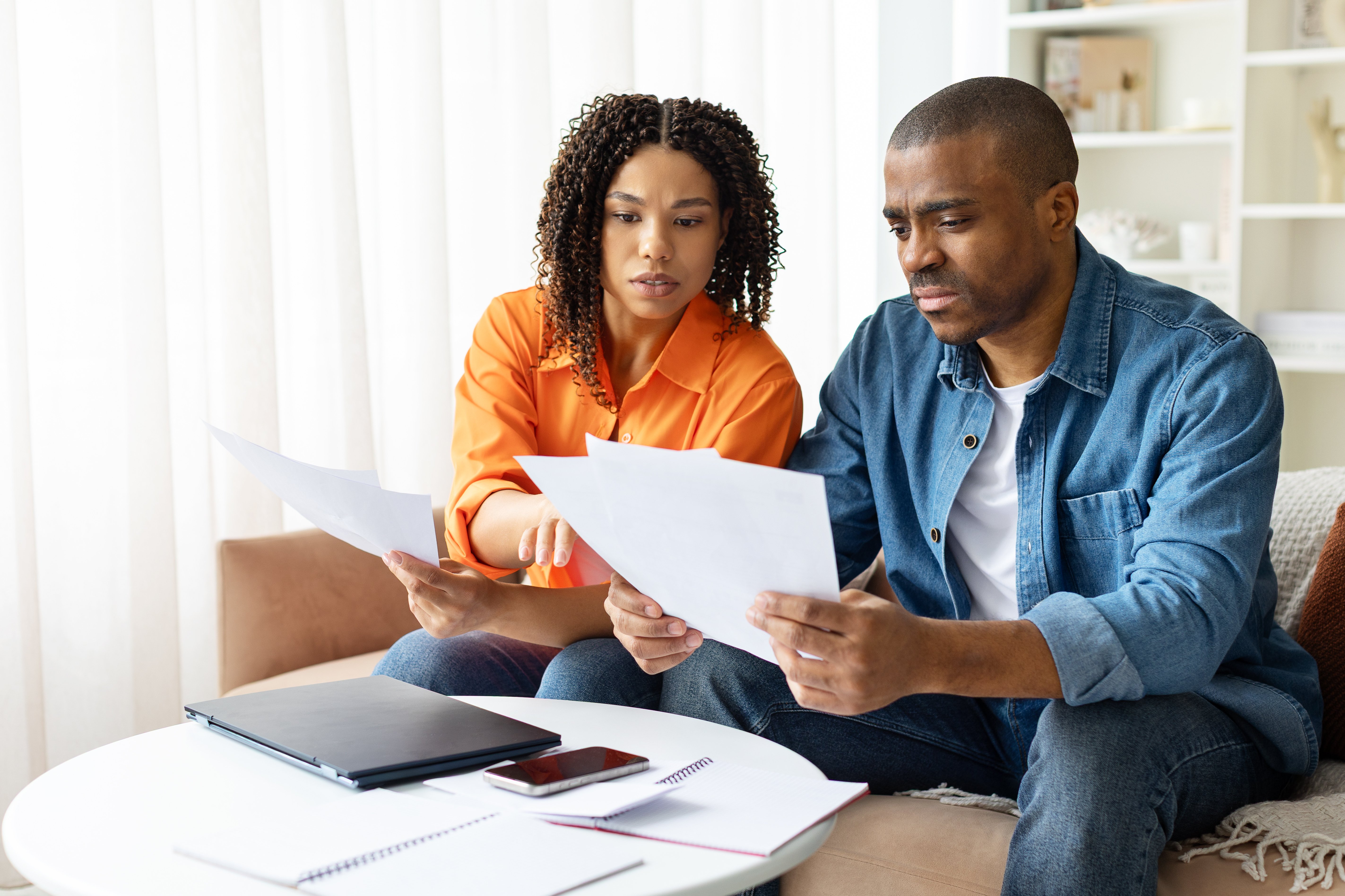 Focused African American couple working on finances at home, reading documents and planning expenses.