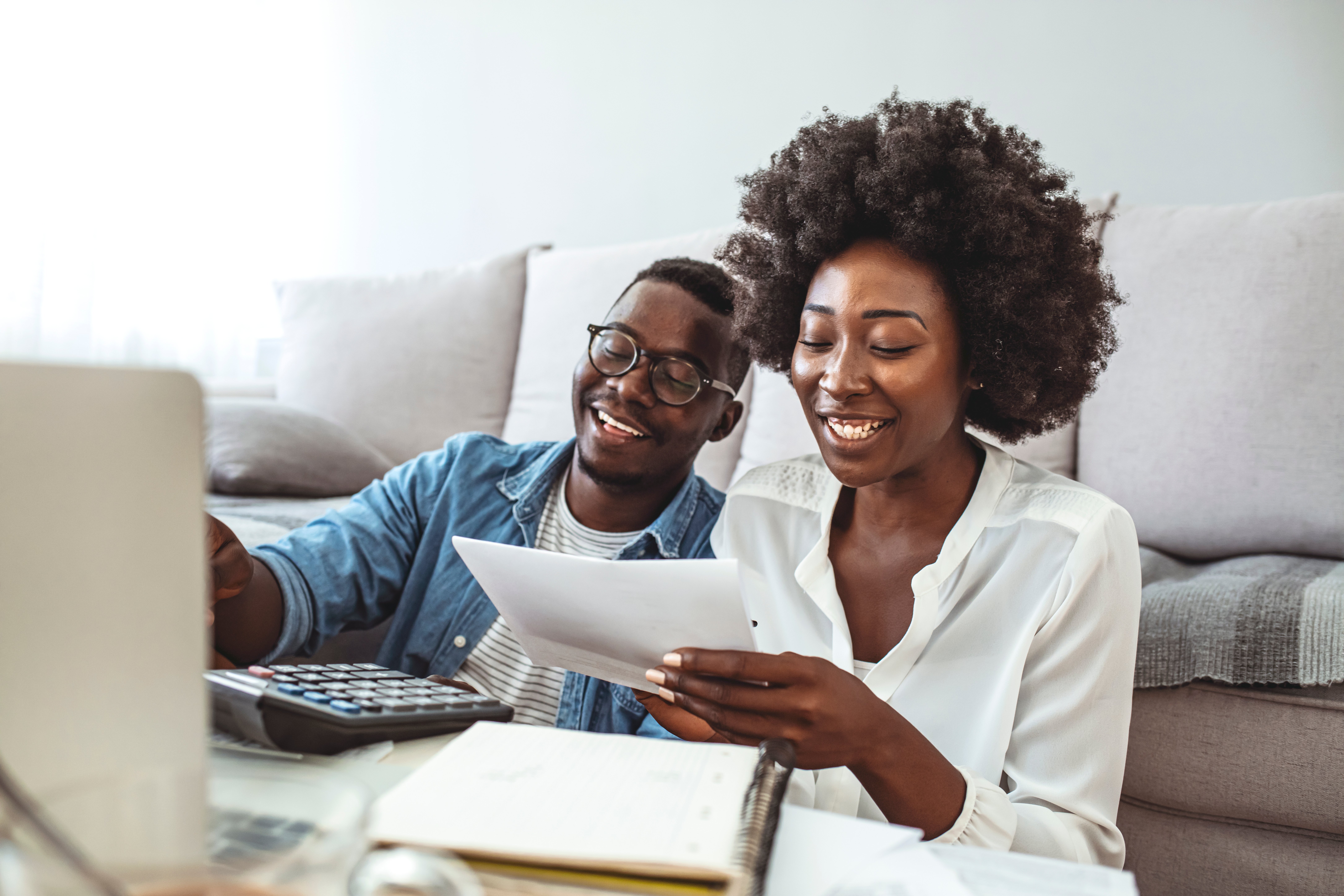 Photo of cheerful loving young couple using laptop and analyzing their finances with documents. Look at papers. Happy couple at home paying bills with laptop
