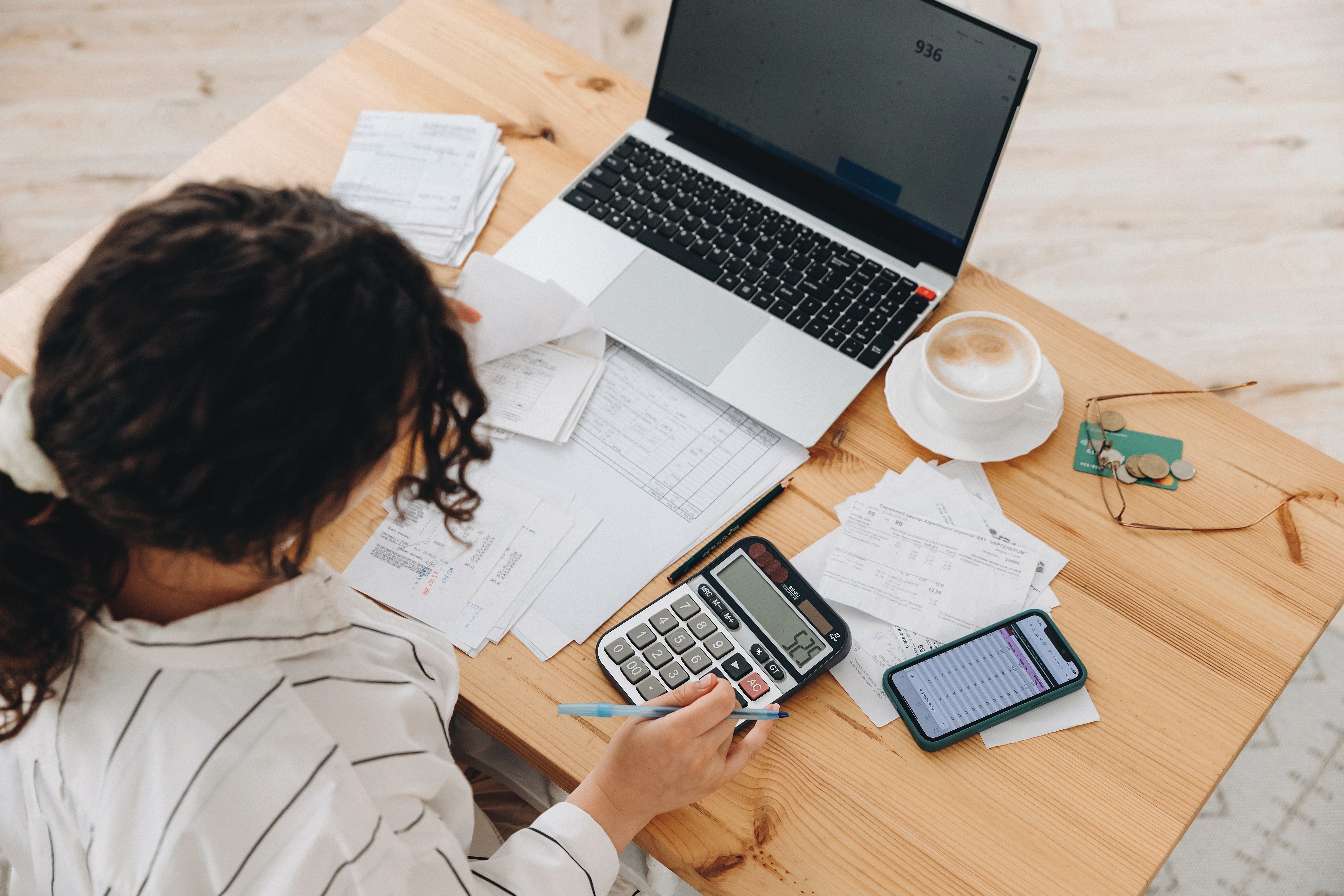 Top view of a woman working at home in the kitchen with financial papers, counting on a calculator, paying bills, planning a budget to save some money