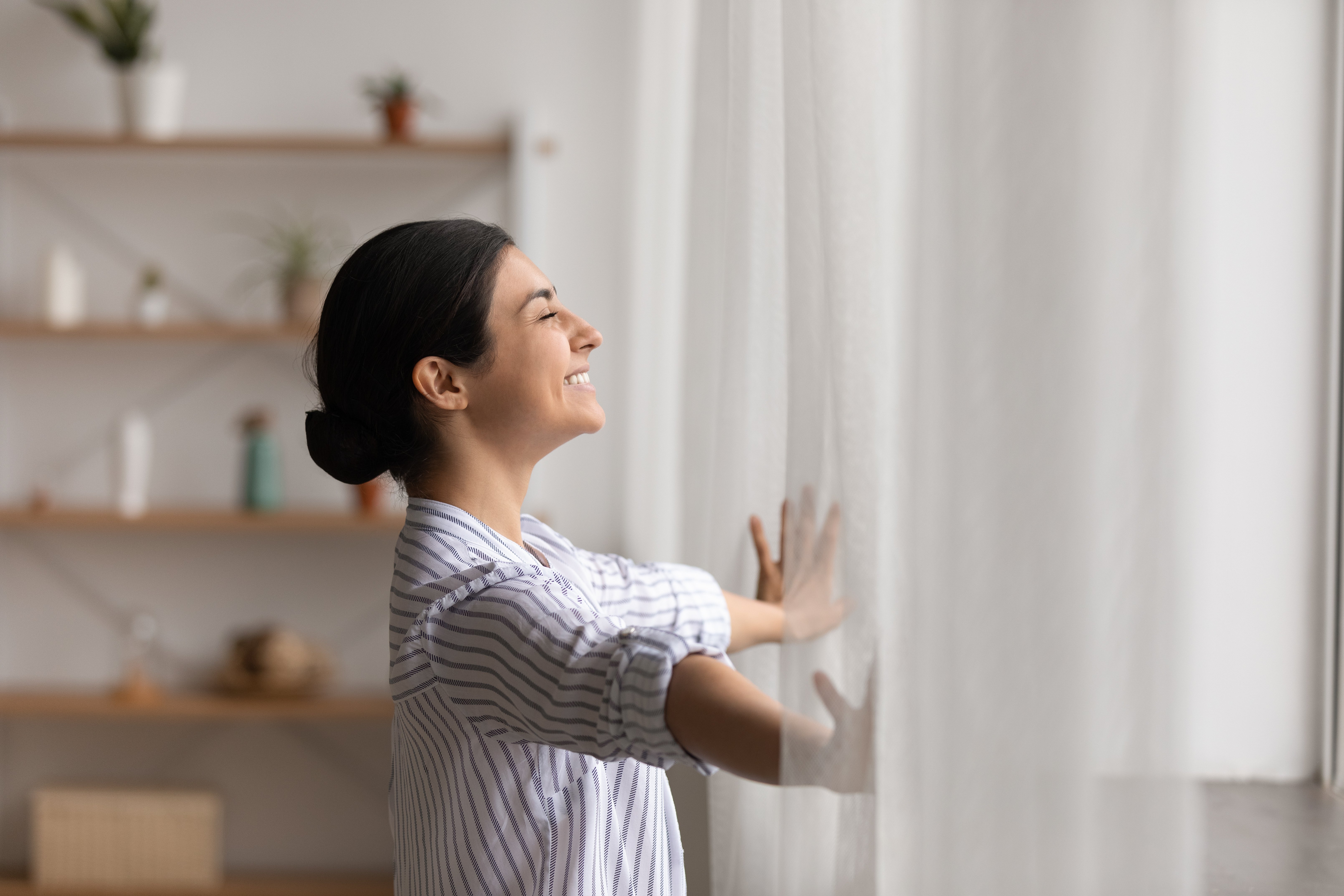 Bathing in sunlight. Excited young indian lady meet first morning at new flat house part curtains enjoy being homeowner.