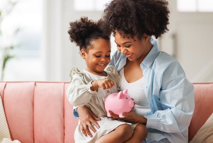 financial education. african american family, mother and child daughter with pig piggy bank counting savings at home.
