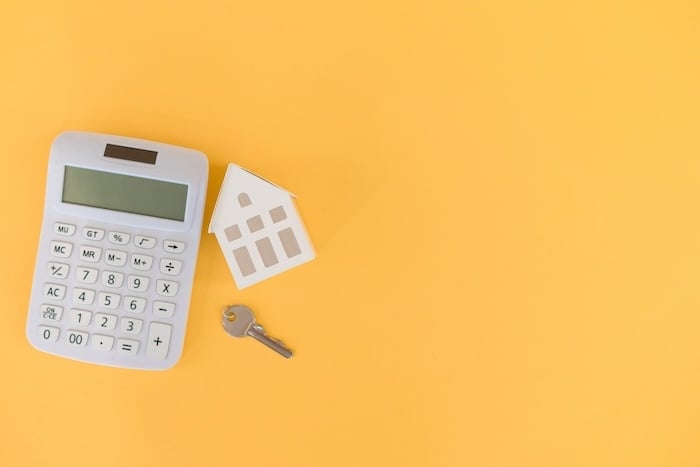 close up top view home model with key and calculator on yellow color background with space for home ownership and buy, sale, rent business financial concept